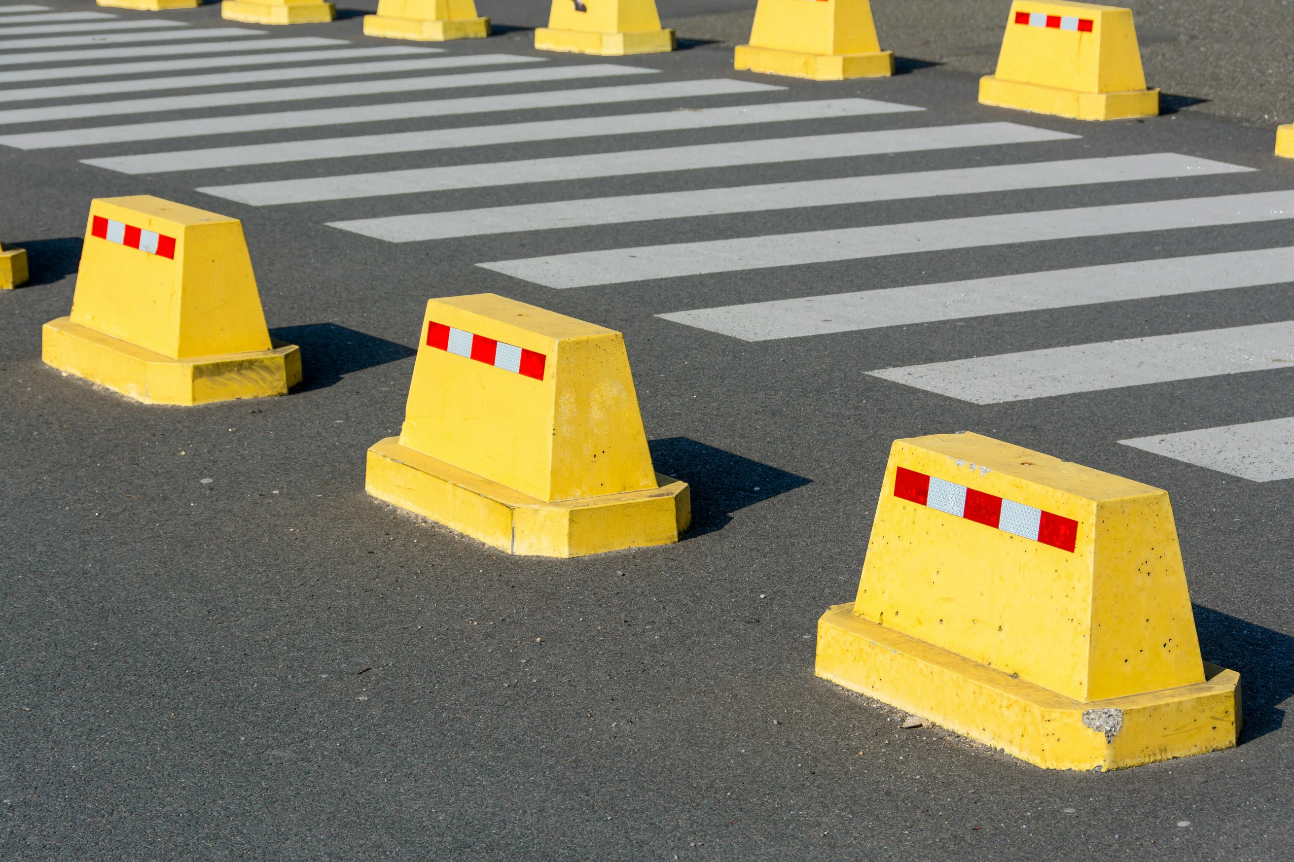 Yellow concrete barriers on asphalt next to a zebra crossing, emphasizing urban street safety.