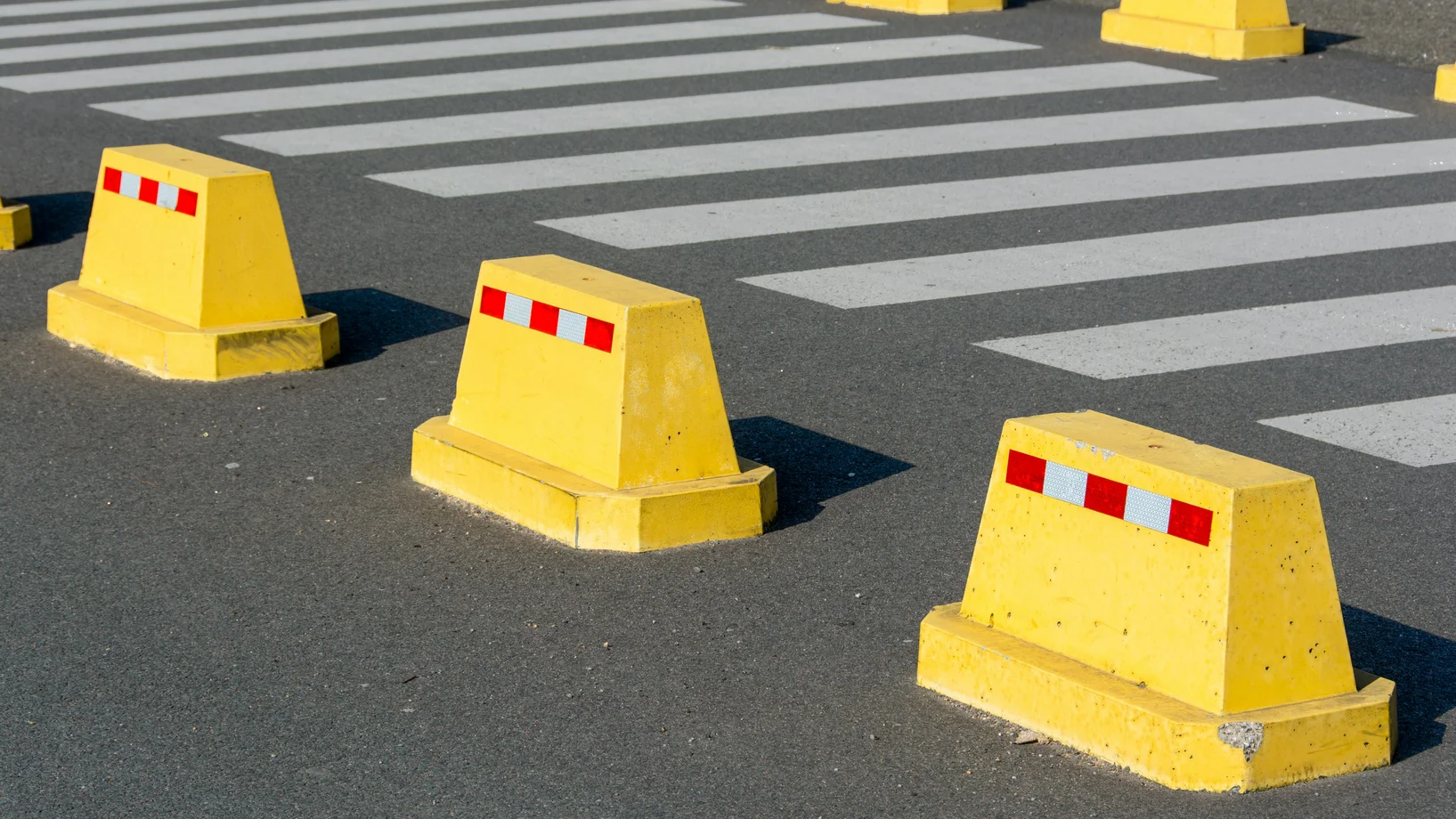 Yellow concrete barriers on asphalt next to a zebra crossing, emphasizing urban street safety.